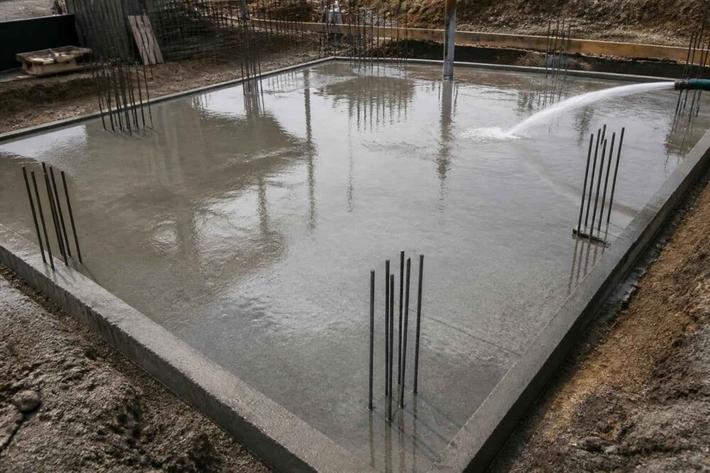 Gładka betonowa płyta fundamentowa z wystającymi prętami zbrojeniowymi na placu budowy